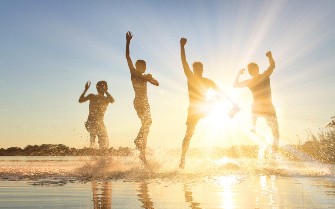 Glückliche junge Menschen laufen und springen am See beim Sonne